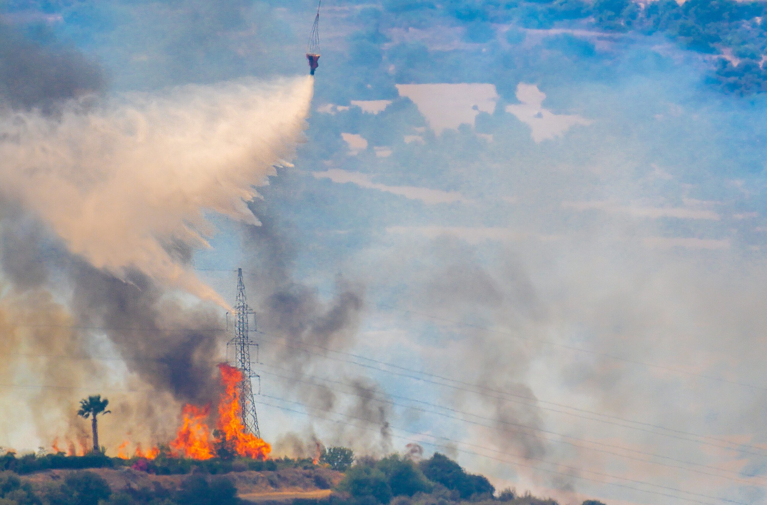 Image of a plane dropping fire retardant on a fire that is next to a power line. 