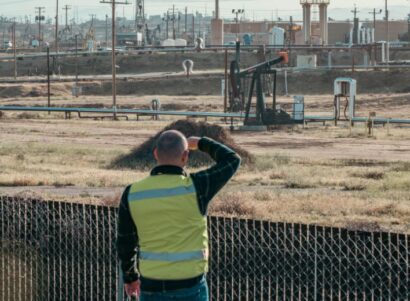 One person looks over the fence at oil and gas infrastructure.