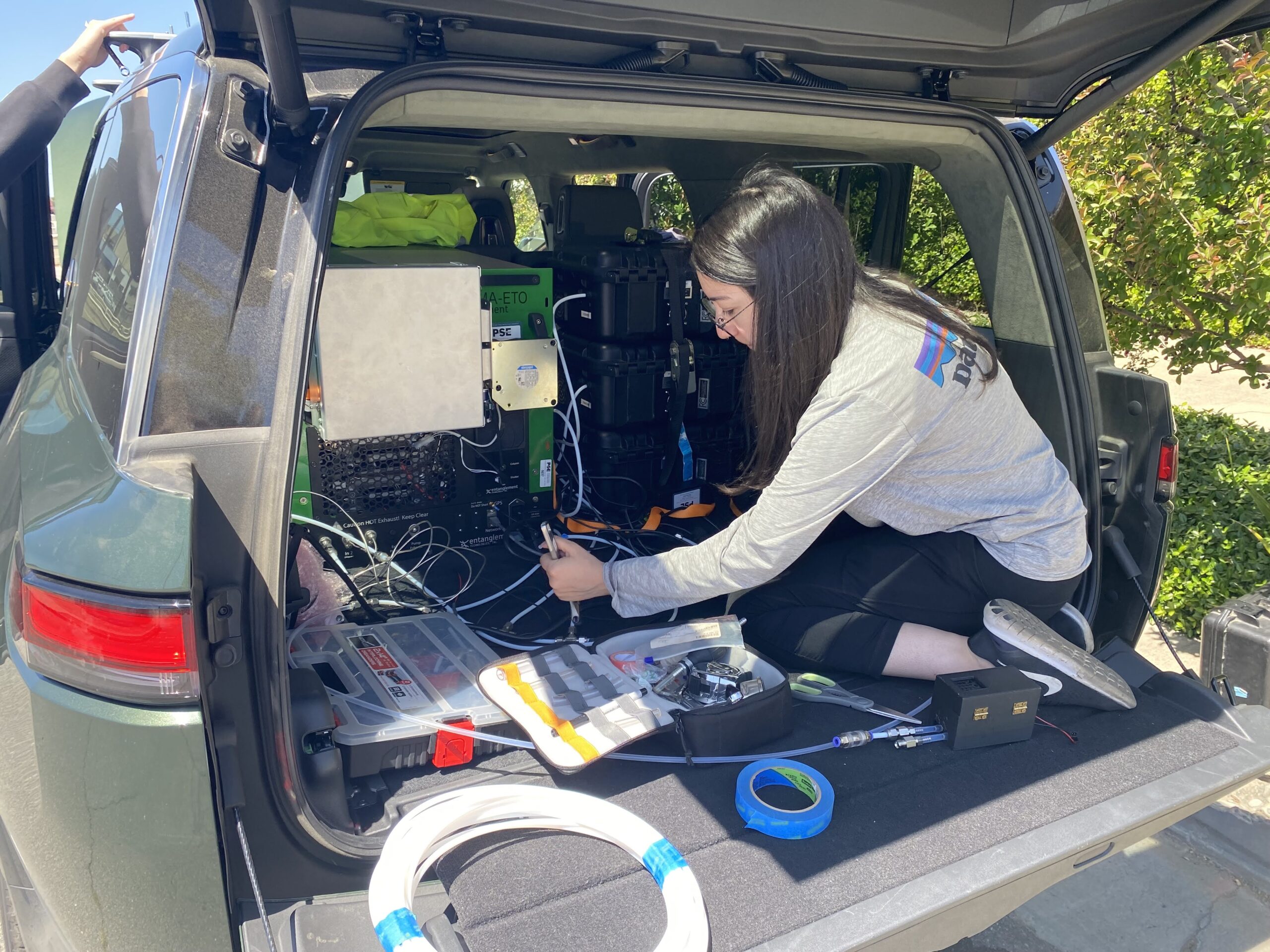 Scientists with analyzers running out of the trunk of a Rivian R1S. 