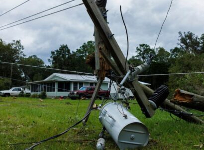 Image of a downed power line on the lawn of a rural home with two cars in the driveway.